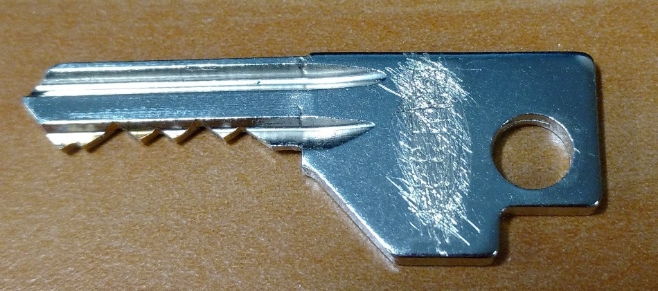 A key with an engraved serial number scratched off. The serial number is now illegible.