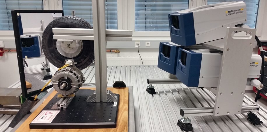 Laboratory Setup. The three Vibrometer Sensor Heads are mounted to a common frame (right side). The roller test bench is to the left with the tire on top and the motor on the bottom. The mirror on the far left is used to simplify the repositioning of the vibrometer scan pattern.
