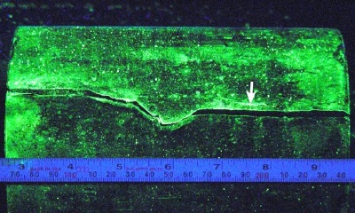 Wet fluorescent magnetic particle indication, arrow, at a secondary crack.